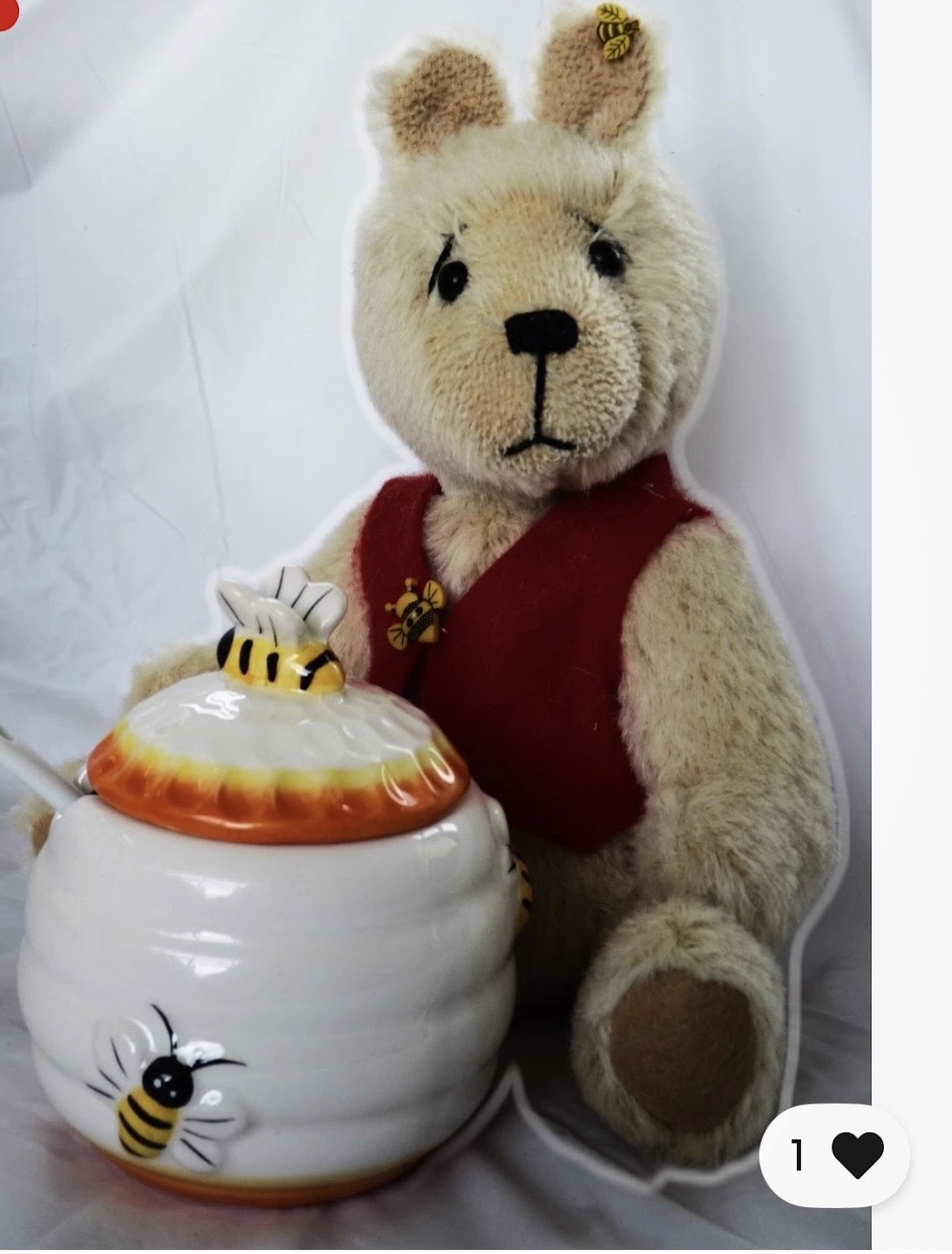 Handmade tan bear wearing a red vest beside a ceramic honey pot